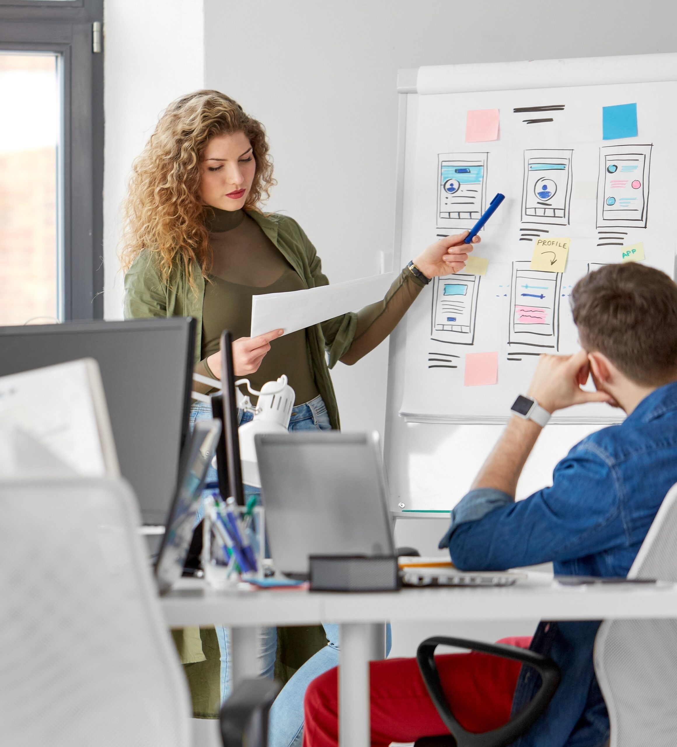 business, technology and people concept - woman showing user interface design on flip chart to creative team at office presentation